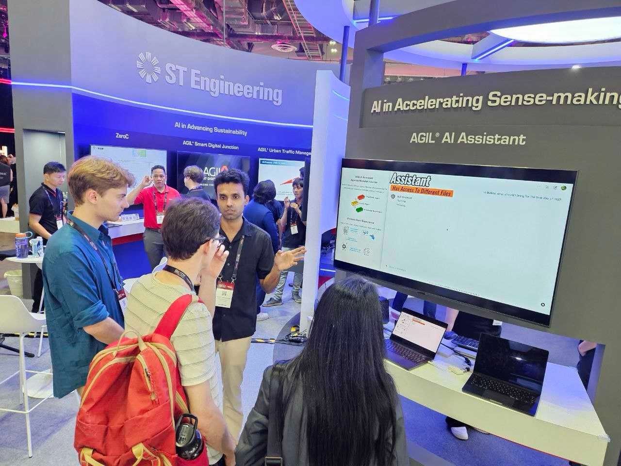 Visitors at the ST Engineering booth watching the AGIL AI Assistant demo on a large screen, under a sign reading “AI in Accelerating Sense-making”